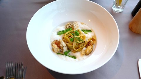 Fresh Pasta Fettuccini with Seafood and Imitation of Sea Foam with Green Peas. Fine Dining Food in Luxury Restaurant - Italian Pasta with Crab Meat in Big White Plate on Table. Delicious Lunch