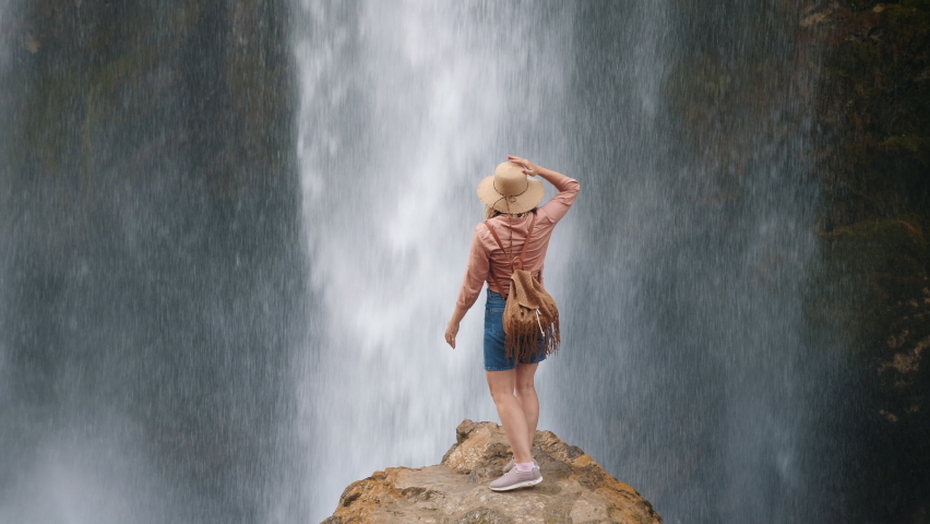 Back view of a young woman traveler enjoying a waterfall while standing on the edge of a stone. Kapuzbasi waterfall Kayseri Turkey