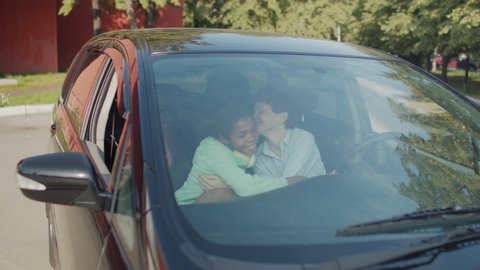 Handheld shot of happy 11-year-old girl with backpack hugging her mother in car and leaving for first day of new school year