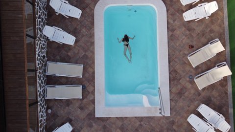Aerial drone shot young woman swimming in clear blue swimming pool water at the hotel. Topdown view on expensive villa house in tropical island.