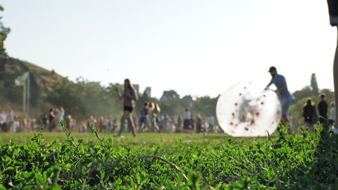 zorbing. zorb ball. inflatable ball. People are having fun. Man is rolling happy child inside large tarsparent inflatable ball on grass, in the park, during festival, city holiday. summer day