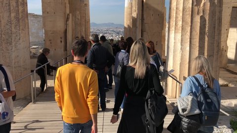 Athens, Greece - 05.03.2021: Many international tourists walking at the Parthenon. Close-up on people. Young woman taking pictures with mobile phone. 4k resolution camera slowly tilt up on columns