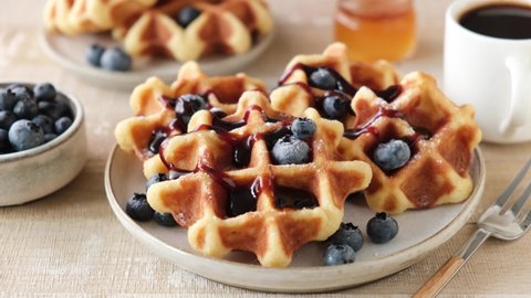 Pouring molasses, amber maple syrup on belgian waffles served with blueberries. Sweet breakfast or dessert closeup view. Tasty food shot