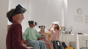 Medium shot of schoolchildren wearing VR headsets and looking around in classroom during lesson - Powered by Shutterstock - Get 15% off with code: PIKWIZARD15