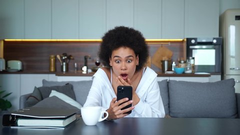Beautiful young mixed race African American woman with mobile phone horrified by the sudden bad news. Upset woman in frustrated feelings from what she saw on the screen of her smartphone