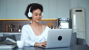 Pretty mixed race African American freelance worker business woman, student of university in wireless headphones talking by video conference via mobile application, greeting her interlocutor .