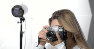 Portrait of a stylish young woman photographer with a long blond hair, makes shots, looking into the camera's video lens and smiling. There is a flash in the background. Professions, hobbies.