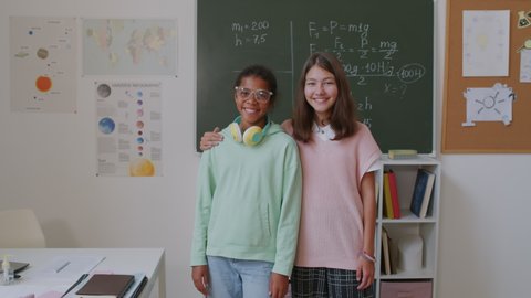 Portrait of happy 11-year-old and 12-year-old girls smiling and posing for camera in classroom