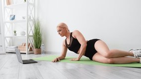 Fitness sport. Athletic woman. Online training. Healthy body. Happy sportive lady in black sportswear doing side plank workout on yoga mat looking laptop light room interior.