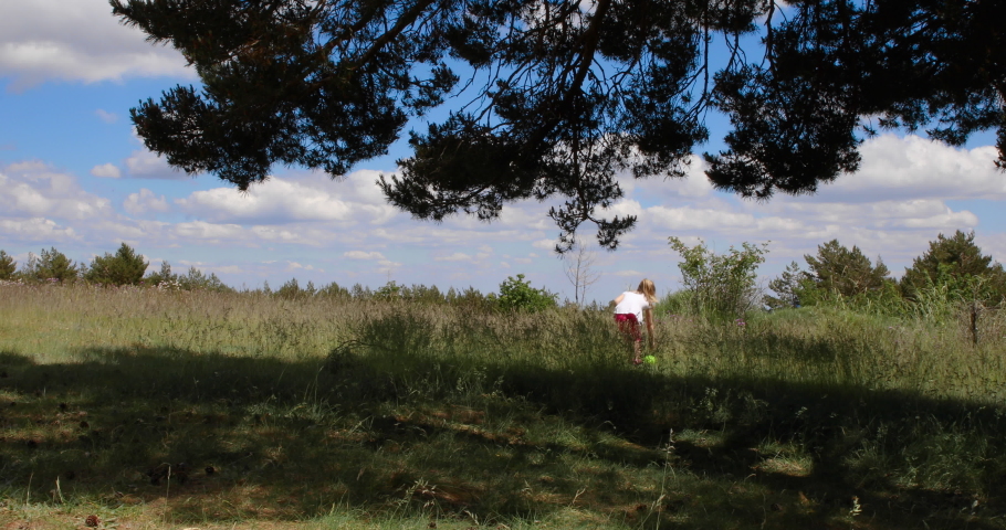 4k video. Four years old blonde girl walking with ball in her hands, next to her mother in meadow of the countryside in Guadarrama, near to Madrid, Spain, Europe

