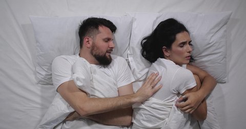 Top view of Caucasian couple quarelling in bed with white sheets. High angle shooting. Man and woman argue, take offense at each other and turn away in different directions