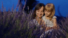 Caucasian mother enjoying time with little child daughter girl, gently touching sniffing aromatic flowers in lavender field. Young pretty woman holding adorable kid on knees sitting in blooming meadow - Powered by Shutterstock - Get 15% off with code: PIKWIZARD15