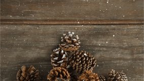 Animation of snow falling over pine cones on wooden table. christmas, winter, tradition and celebration concept digitally generated video.