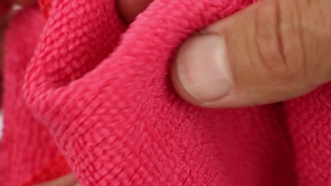 hands testing, crushes and stretches red microfiber dusting cloth, well-absorbing water synthetic fabric, close-up view on texture of textile