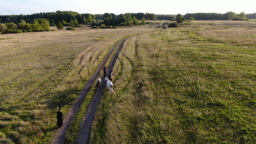 Two men lead the horses home through the field in the evening