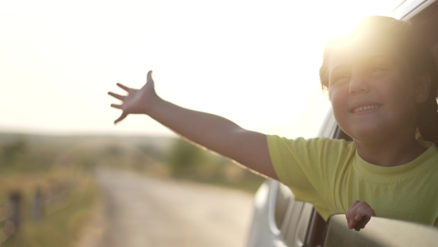 Child in car window. Family car trip. Child hair in wind. Girl looks out of car window. Happy child travel with his family. Girl stretches out his hand to wind. Happy family travel concept by car | Shutterstock HD Video #1078553942