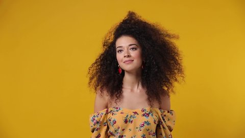 Charming overjoyed excited jubilant exultant young latin curly woman 20s wears casual flower dress dance waving fooling around have fun enjoy play fluttering hair isolated on plain yellow background