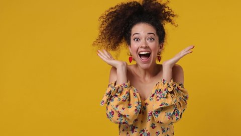 Joyful jubilant surprised shocked charming vivid fun young latin curly woman 20s wears casual flower dress say wow omg what spreading hands put arms on face screech isolated on plain yellow background
