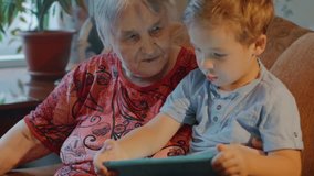 Slow motion clip of grandmother and grandson using tablet for entertainment while sitting on the sofa at home