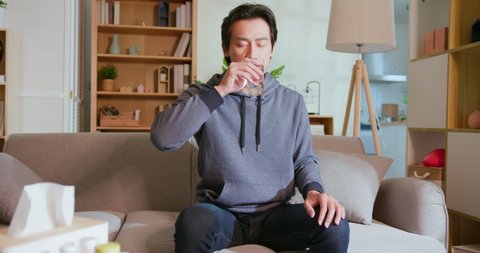 asian man takes medicine or vitamin by water in living room at home