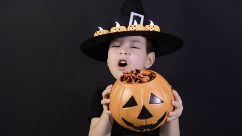 A Halloween child holds a pumpkin with candy and screams, sings songs. Preparation for the holiday