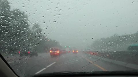 JAKARTA, INDONESIA - SEPTEMBER 3, 2021: Driving a car on a highway toll road during a heavy rainstorm with driver POV on front seat rain drops water hitting front car window on a dark sky bad weather 