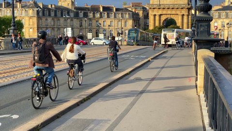 Bordeaux, France - August 2021 : Trams and tourists on bicycles crossing the Pont de Pierre bridge in the streets of Bordeaux, France