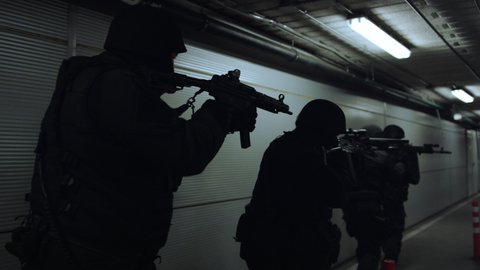 SWAT team with automatic rifles walking in dark corridor. Special forces group pointing weapons. Military soldiers storming building during mission. Anti-terrorist squad inspecting territory