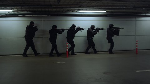 Dolly shot of SWAT police officers walking on underground parking with weapons. Special forces aiming assault rifles during military operation. Anti terrorist squad investigating building at night