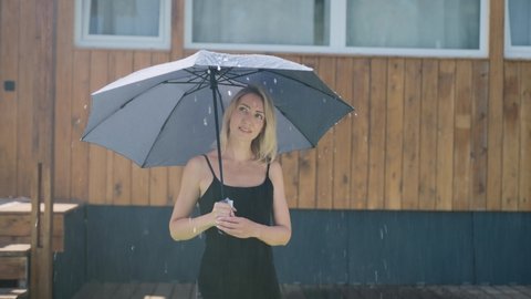 Attractive blonde in the summer rain. A pretty woman uses an umbrella to protect herself from a rainstorm.