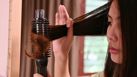 Asian woman curling hair with hair curler fashion with herself in front of mirror in bedroom
