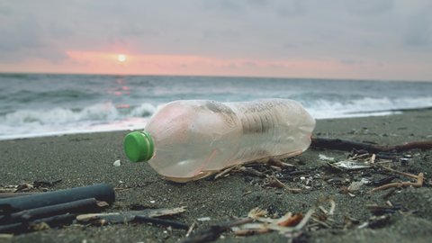 Discarded plastic bottle on the sandy shore near waving sea on sunset.