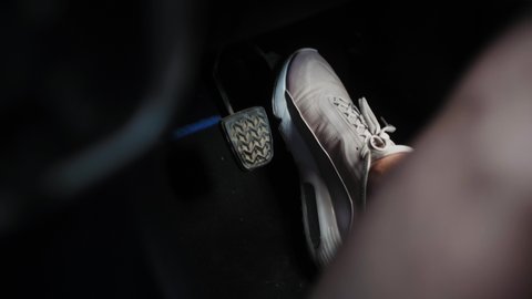 Foot in sneaker pressing gas pedal in car, close-up view.