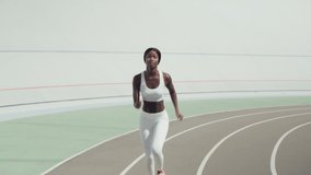 Confident young African woman in sports clothing running on track outdoors