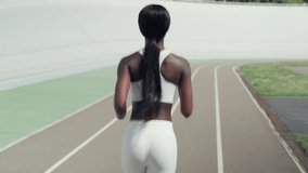 Rear view of beautiful young African woman in sports clothing running on track