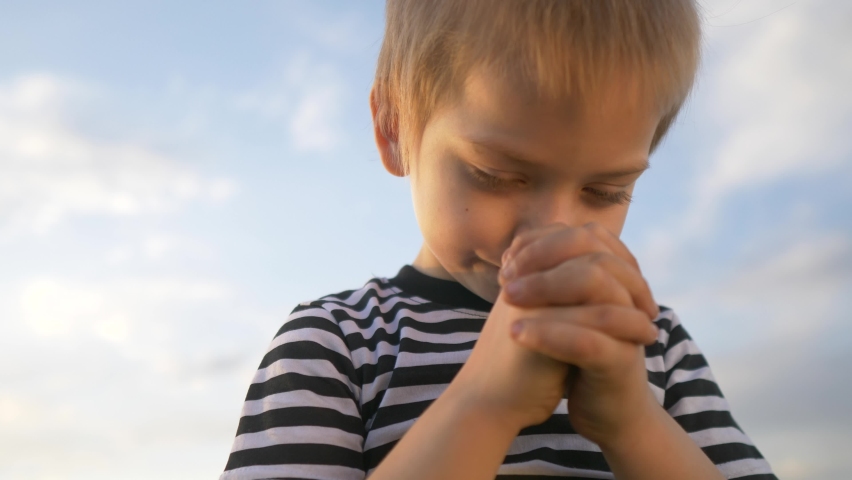 boy prays against a blue sky. child close-up concept faith religion lifestyle and happy family. kid son jew crossed arms praying to god. worship and gratitude for life and a happy childhood. catholic Royalty-Free Stock Footage #1078586102