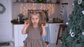 4k video portrait of happy proud little baby girl making tasty Christmas sweets in holiday decorated kitchen background. Chid holding in hands raw gingerbread cookies showing them into camera