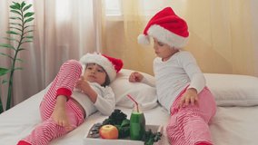 Cute Children in Santa's hats drink healthy fruity green cocktail in the morning. Happy children in the apartment celebrate the New Year and have breakfast with fresh fruits and vegetables