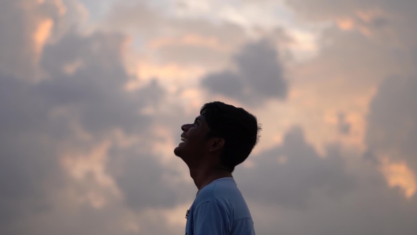 Portrait of an Indian kid happily looking at the orange sky with clouds during the sunset. Hopeful kid looking at the sky and smiling | Shutterstock HD Video #1078600256