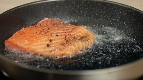Salmon steak is placed on a frying pan and fried. Slow motion video of cooking diet fish in the kitchen at home.