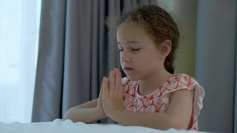 Little girl is praying in her room.Close up portrait of child concept faith religion and happy family.Child daughter crossed her arms, praying to god.Catholic pray worship and gratitude.