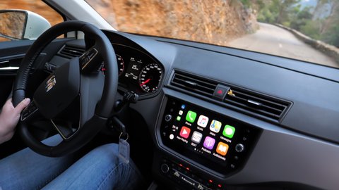 Mallorca, Spain - Circa 2020: Woman driving Seat car with Apple CarPlay dashboard on with Apps of iPhone, Music, Maps Messages, YouTube Sear and Podcast Audiobooks - difficult mountain serpentine road