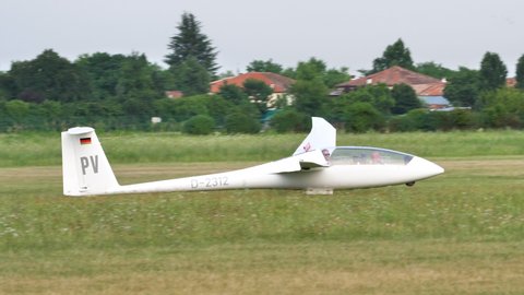 Thiene, Italy JULY, 8, 2021 Sailplane slows and stops after landing in a small airport with a grass runway and a church in the background. Schempp-Hirth Duo Discus