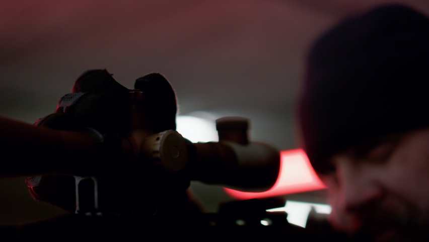 Professional killer holding sniper rifle. Closeup serious gunman looking through scope of modern firearm. Male terrorist shooting with weapon. Dangerous man with gun on position