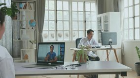 Asian Woman Doctor Having Video Conference On Laptop Computer In Workplace With Man Patient On Screen Display. Medical Concept

