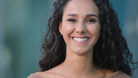 Portrait outdoors close up beautiful stylish hispanic arabian caucasian woman curly brunette girl smiling at camera looking confident. Happy lady smile urban city background. Real people concept