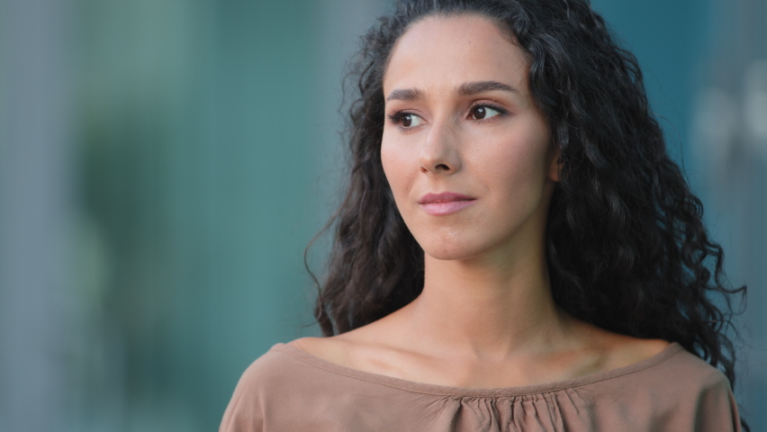 Outdoors portrait female face with perfect skin make-up hispanic woman young adult pensive girl standing in city building background looks to side turns head looking at camera smiling toothy smile Royalty-Free Stock Footage #1078636742