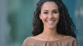 Outdoors portrait female face with perfect skin make-up hispanic woman young adult pensive girl standing in city building background looks to side turns head looking at camera smiling toothy smile - Powered by Shutterstock - Get 15% off with code: PIKWIZARD15