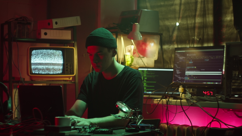 Hacker typing on keyboard at night, breaking password, using laptop and bypassing cybersecurity. Young man developing program in dark room. Programmer infecting system with cyber virus