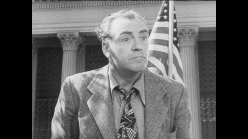 1940s: Man speaking in front of flag. Men in hats talking. Man talking. Man on box delivering speech to audience in park. Man waving hand in dismissal, sneering, walking away.